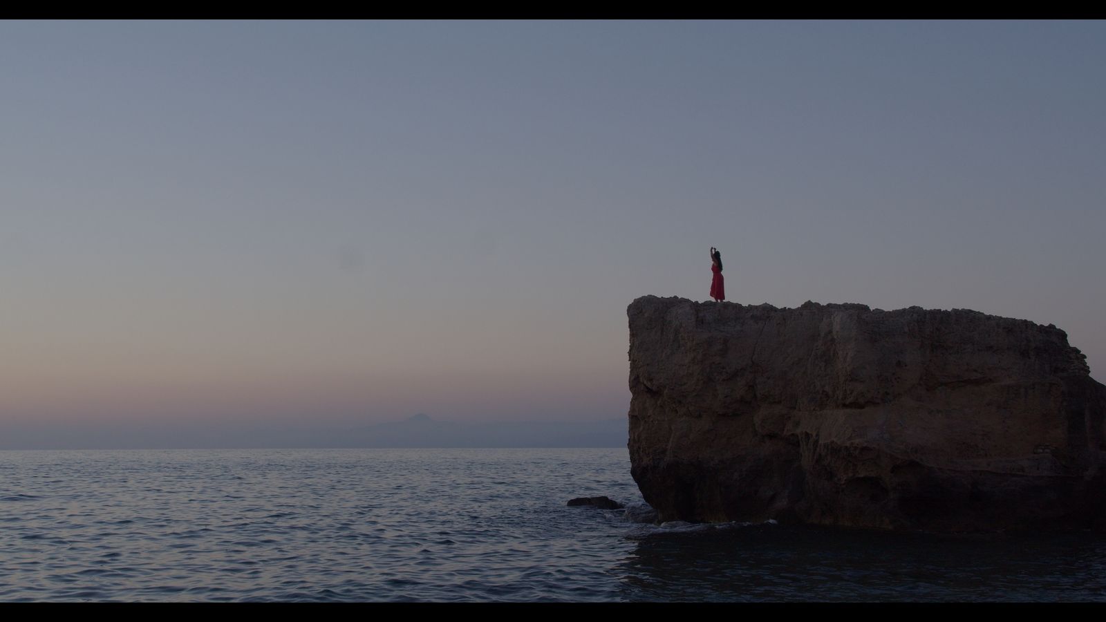 Una figura in rosso su uno scoglio al tramonto